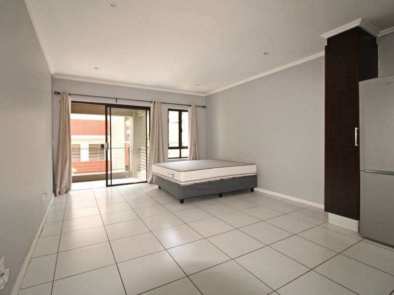 An open-plan living area featuring tiled flooring, recessed lighting, and a sliding door leading to a balcony, with a built-in storage cupboard.