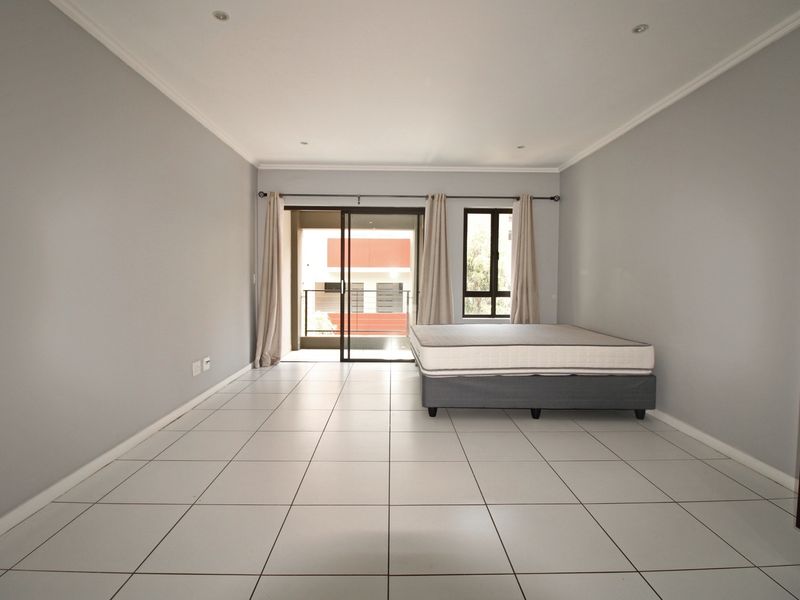 Spacious bedroom featuring neutral grey walls, white tiled flooring, recessed lighting, and direct access to a private balcony through a sliding glass door.