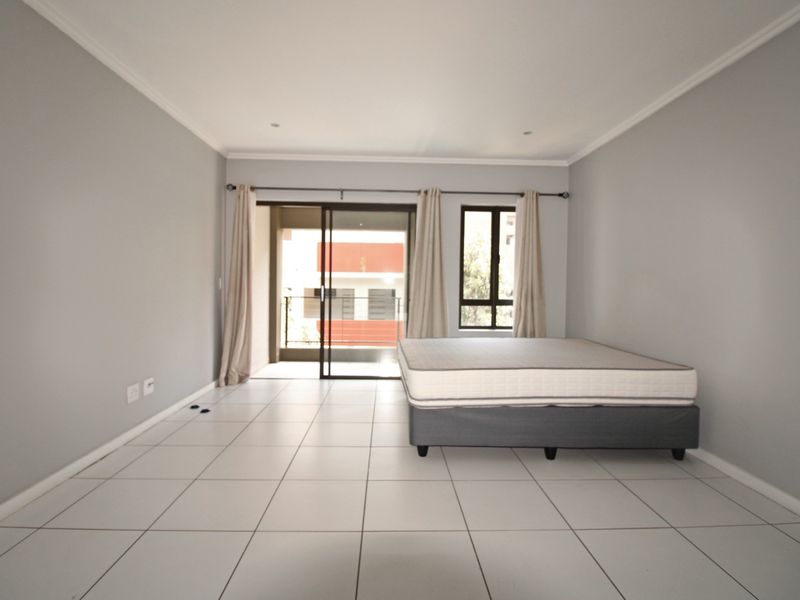 Spacious bedroom featuring neutral tiled flooring, recessed lighting, and direct access to a private balcony through a sliding glass door.