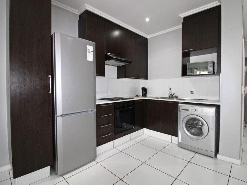 Modern kitchen featuring dark wood cabinetry, built-in oven, hob, extractor fan, and tiled flooring with space for integrated appliances.