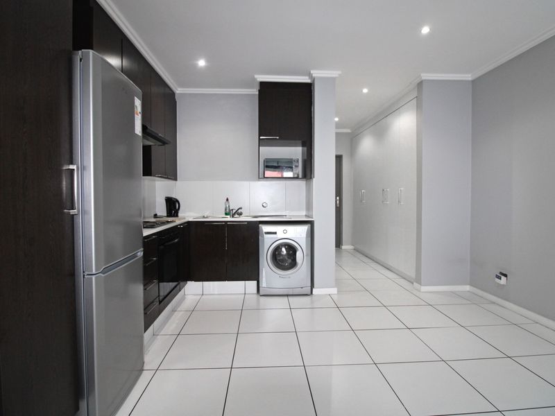 Modern kitchen featuring dark cabinetry, tiled flooring, integrated appliances, and ample built-in storage, seamlessly flowing into the adjacent living area.