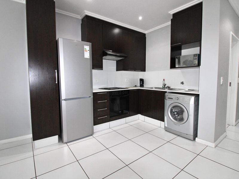 Modern kitchen featuring dark wood cabinetry, built-in oven, hob, extractor fan, and tiled flooring with a clean, functional layout.