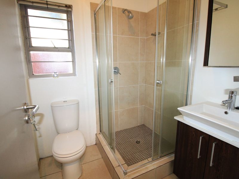 A functional bathroom featuring a glass-enclosed shower, a modern vanity with basin, and neutral wall and floor tiling.