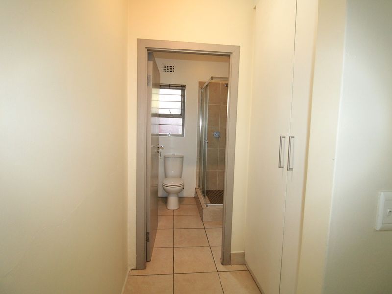 A functional bathroom featuring a shower enclosure, toilet, tiled flooring, and adjacent built-in storage cupboards.