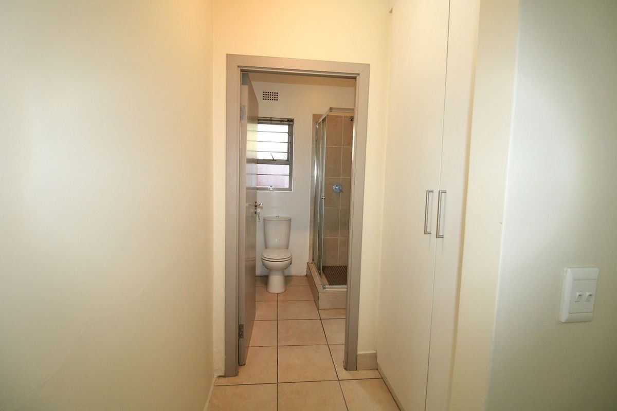 A functional bathroom featuring a shower enclosure, toilet, tiled flooring, and adjacent built-in storage cupboards.