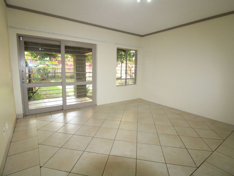 A bright, empty living area featuring neutral tiled flooring and large sliding glass doors that provide direct access to the garden.