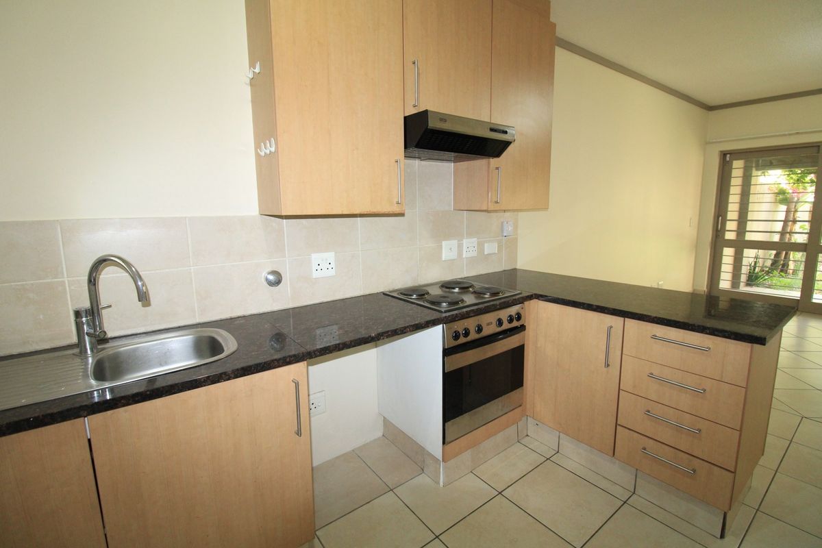 A functional kitchen featuring light wood cabinetry, dark granite countertops, built-in oven and hob, and tiled flooring, offering a clean and practical workspace.