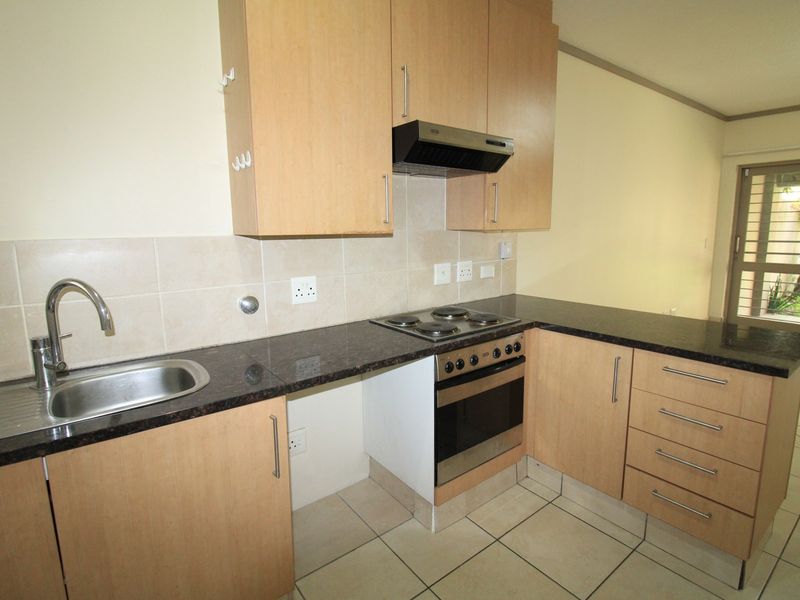 A functional kitchen featuring light wood cabinetry, dark granite countertops, built-in oven and hob, and tiled flooring, offering a clean and practical workspace.