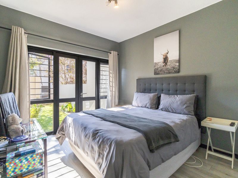 A well-lit bedroom featuring modern laminate flooring and large glass sliding doors providing direct access to the garden area.