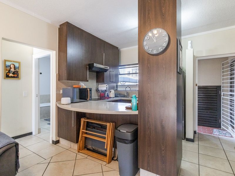 A compact kitchen featuring dark wood cabinetry, stone countertops, and tiled flooring, with an open layout connecting to adjacent living and hallway areas.