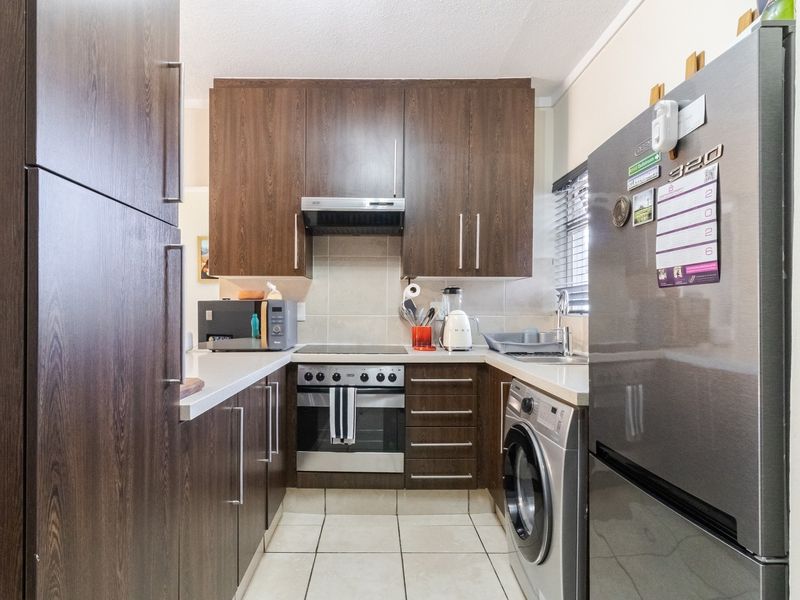 A compact, functional kitchen featuring dark wood-finish cabinetry, stainless steel appliances, tiled flooring, and integrated laundry plumbing for efficient space utilization.