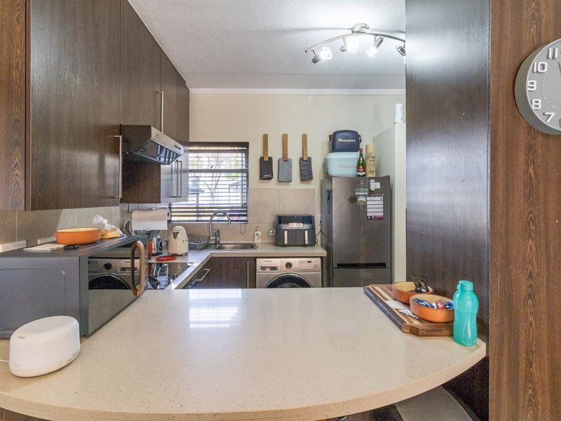 Compact kitchen featuring dark wood cabinetry, stone countertops, a tiled backsplash, and integrated appliances, offering a functional and efficient workspace.