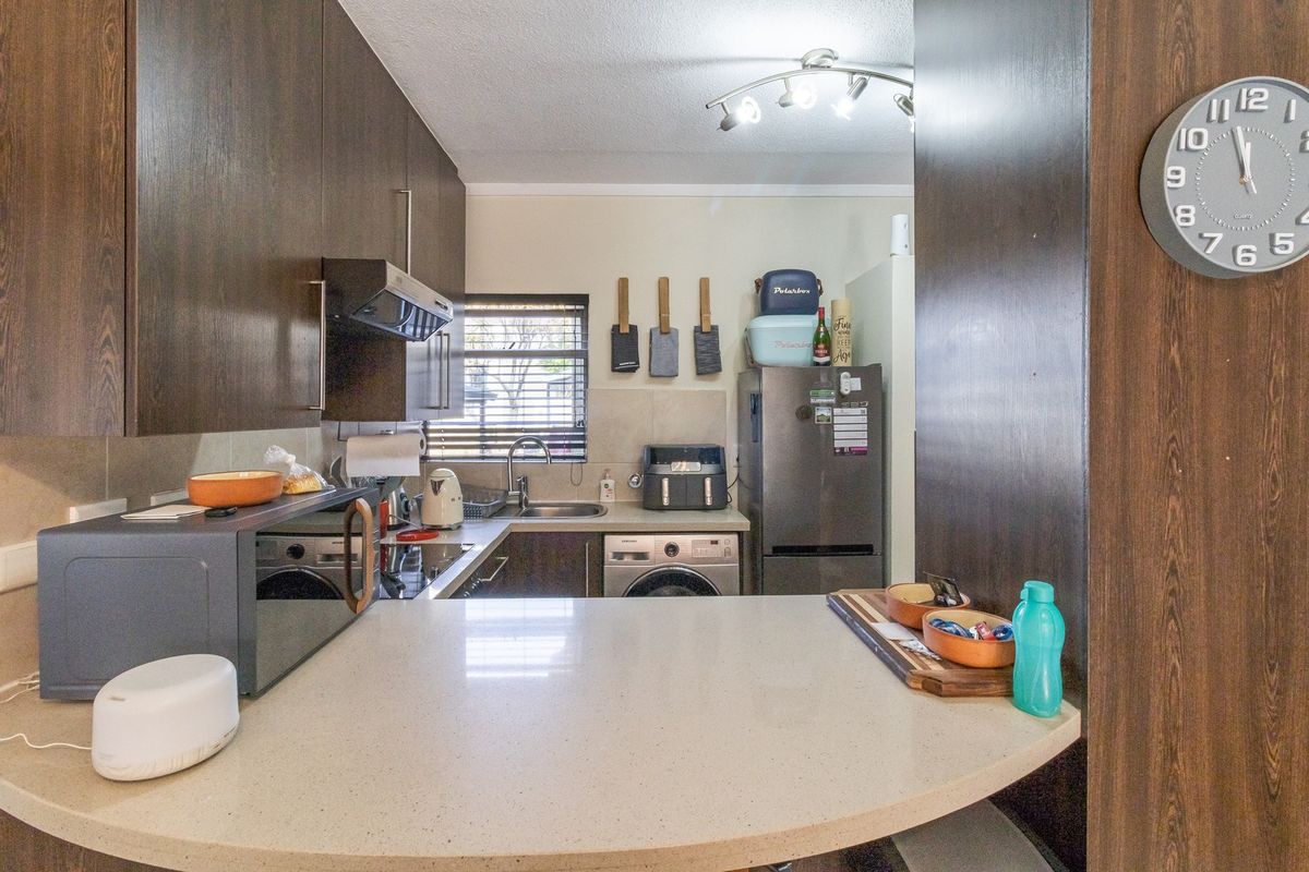 Compact kitchen featuring dark wood cabinetry, stone countertops, a tiled backsplash, and integrated appliances, offering a functional and efficient workspace.