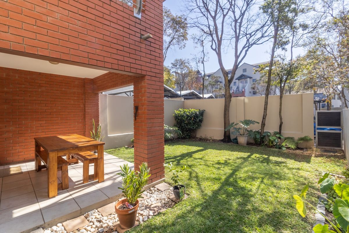 A private rear garden featuring a covered brick patio area and a well-maintained lawn enclosed by boundary walls.