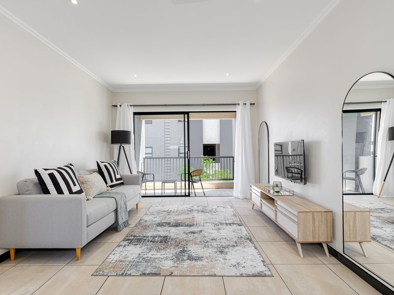 A bright and modern living room featuring tiled flooring, recessed lighting, and direct access to a private balcony through sliding glass doors.