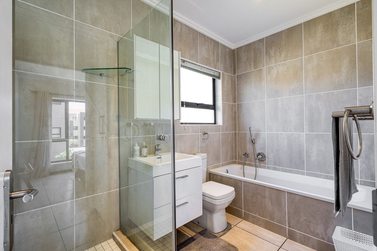 Modern bathroom featuring a glass-enclosed shower, built-in vanity with storage, and a bathtub with neutral floor-to-ceiling tiling.
