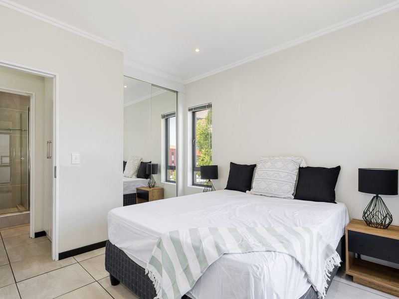 A well-maintained bedroom featuring tiled flooring, recessed lighting, and a mirrored built-in wardrobe, with convenient access to an adjoining en-suite bathroom.