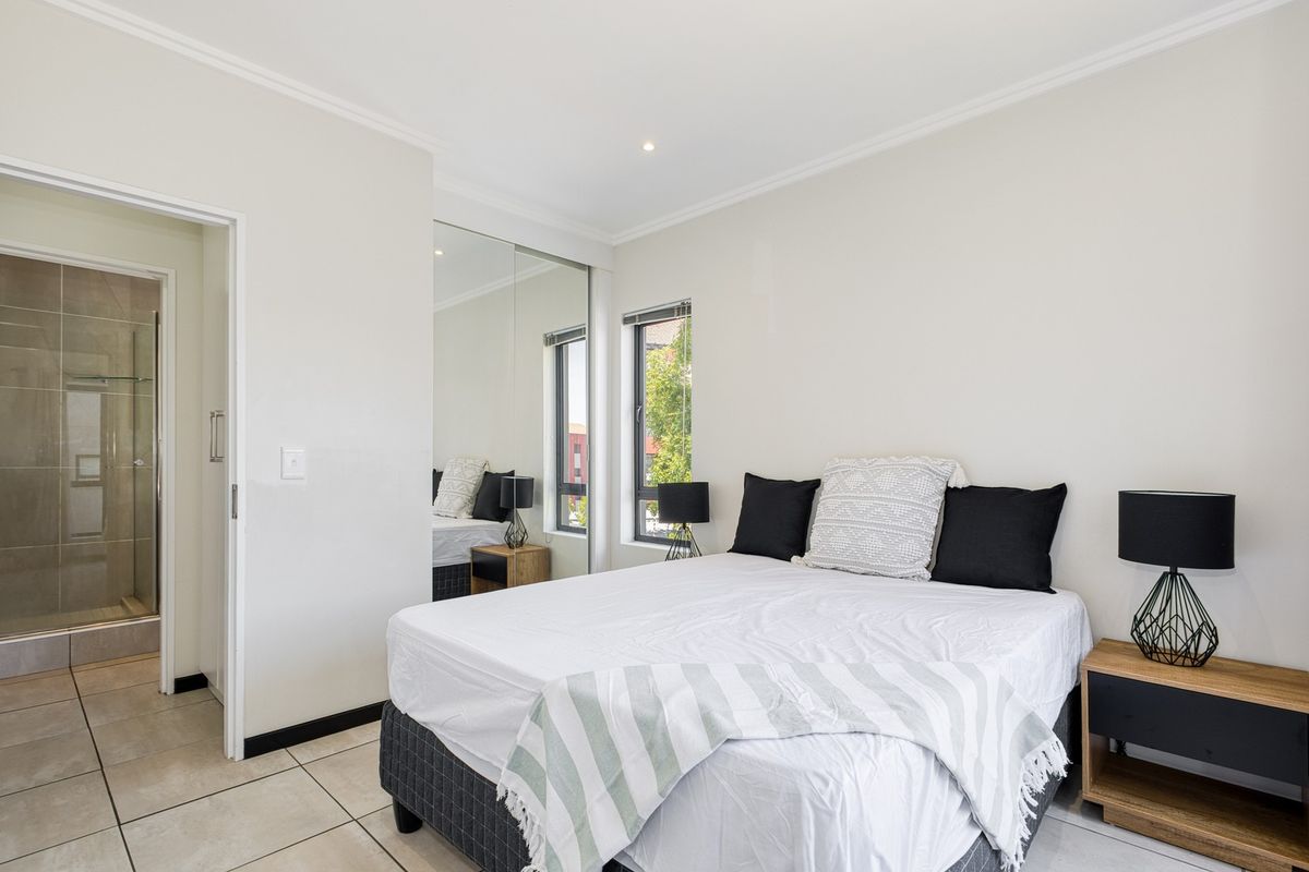 A well-maintained bedroom featuring tiled flooring, recessed lighting, and a mirrored built-in wardrobe, with convenient access to an adjoining en-suite bathroom.