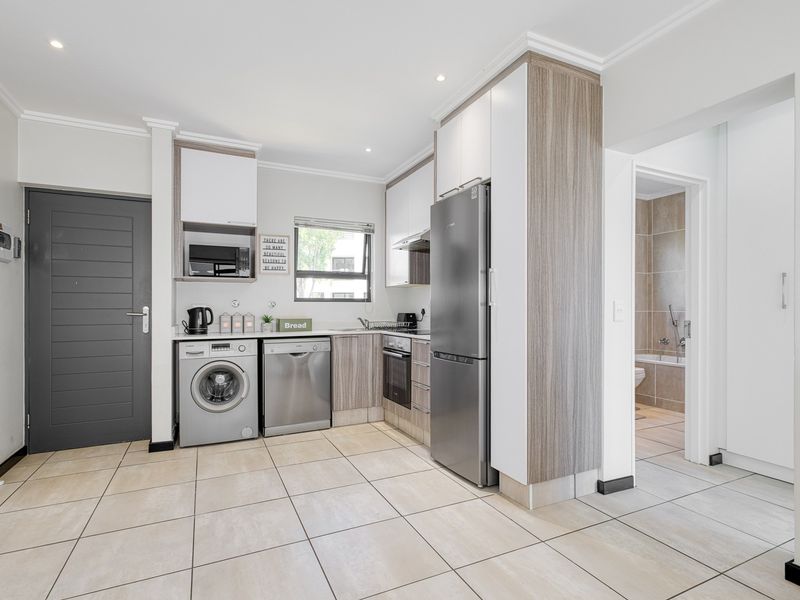 Modern kitchen featuring sleek wood-grain and white cabinetry, integrated appliances, tiled flooring, and recessed lighting, with direct access to an adjacent bathroom.
