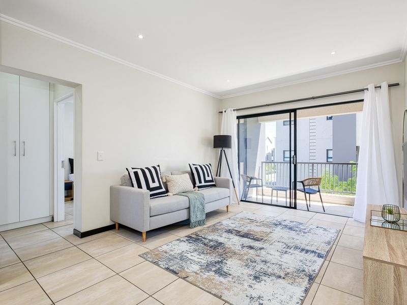 A bright and modern living room featuring tiled floors, recessed lighting, and large sliding glass doors that open onto a private balcony.