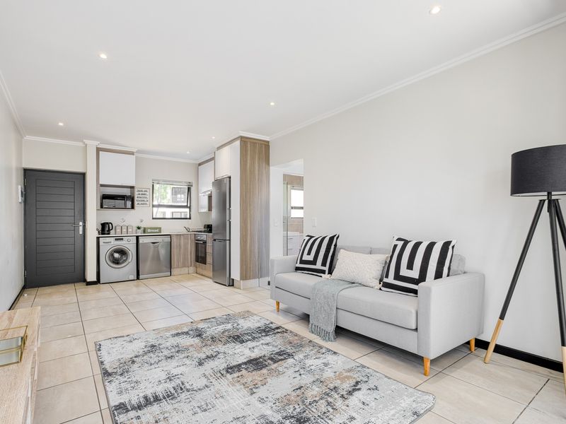 An open-plan living area featuring a modern kitchen with built-in cabinetry, tiled flooring, and recessed lighting, seamlessly integrated with the lounge space.