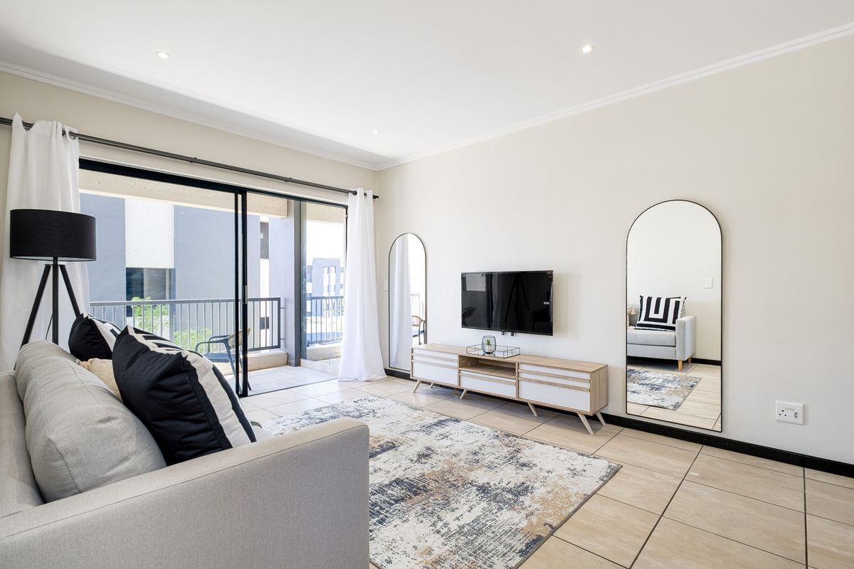 A bright and modern living room featuring tiled floors, recessed lighting, and large sliding glass doors that open onto a private balcony.