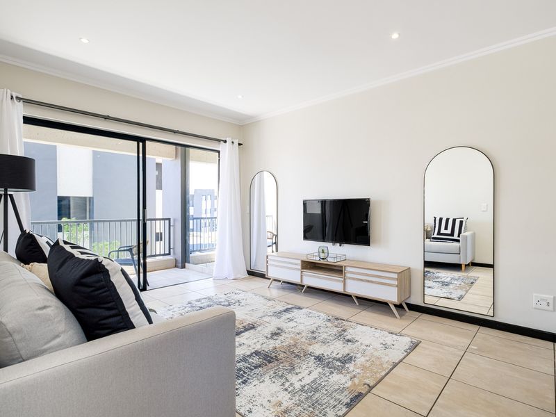 A bright and modern living room featuring tiled floors, recessed lighting, and large sliding glass doors that open onto a private balcony.