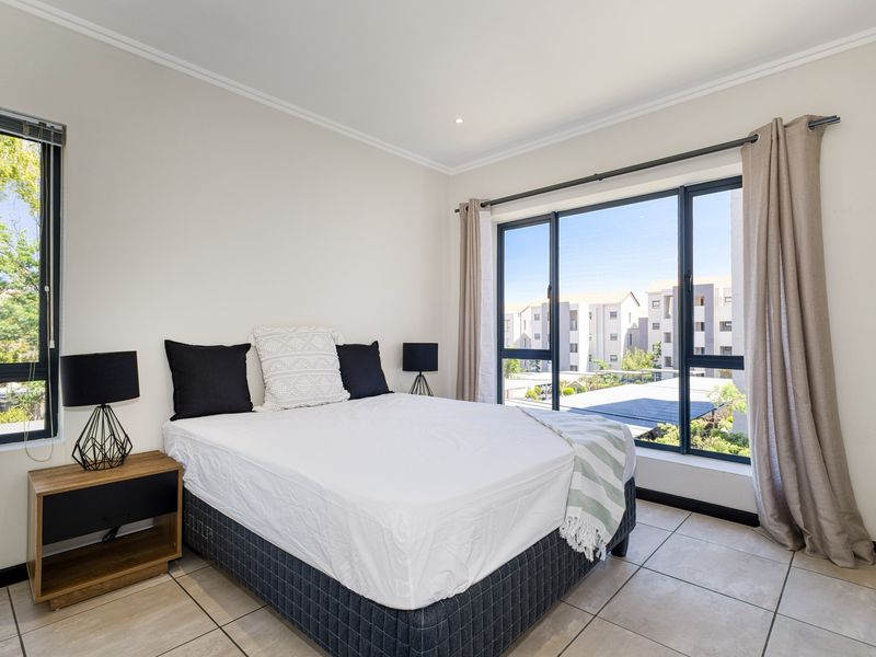 A bright and well-maintained bedroom featuring large aluminium-framed windows, neutral tiled flooring, and recessed downlighting, offering a clean and modern living space.