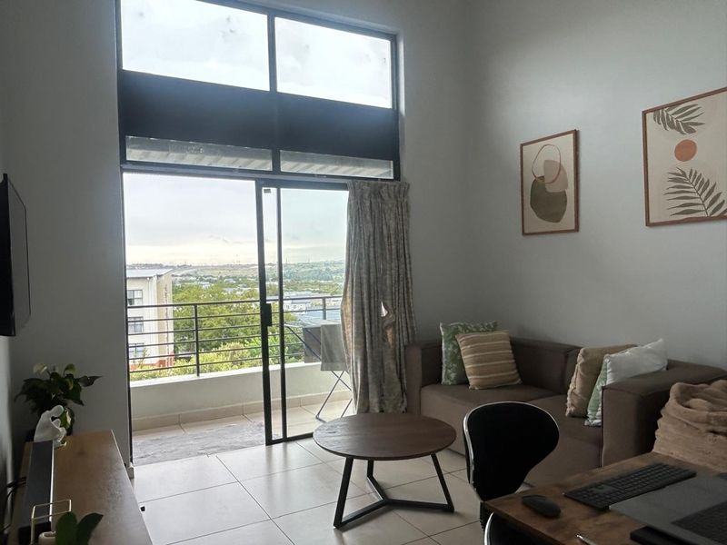 A bright living room featuring large windows and a sliding glass door that opens onto a balcony with scenic views.