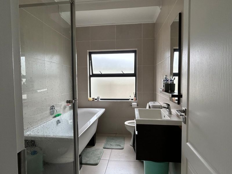 A modern bathroom featuring a freestanding bathtub, glass-enclosed shower, wall-mounted vanity with basin, and neutral floor-to-ceiling tiling.