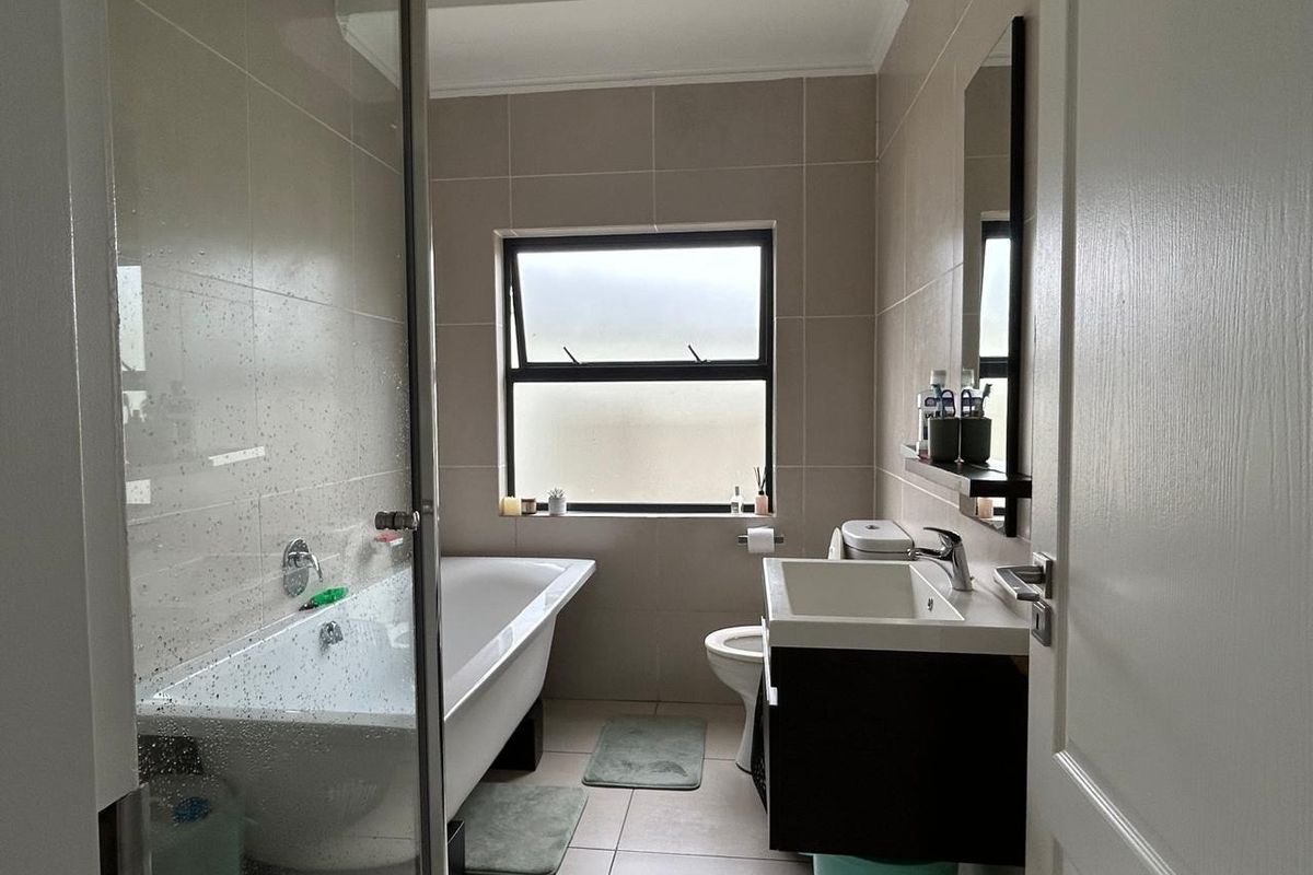A modern bathroom featuring a freestanding bathtub, glass-enclosed shower, wall-mounted vanity with basin, and neutral floor-to-ceiling tiling.
