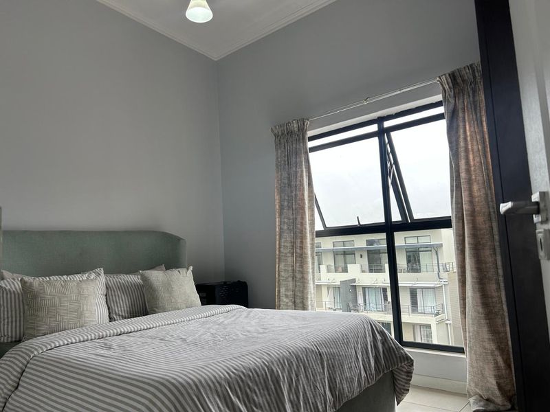 A well-lit bedroom featuring neutral wall tones, a large aluminium-framed window, and classic ceiling cornice detailing.