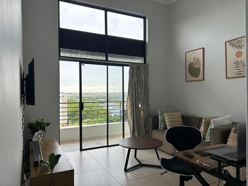 Bright living room featuring large sliding glass doors with transom windows, providing balcony access and scenic views with neutral tiled flooring throughout.