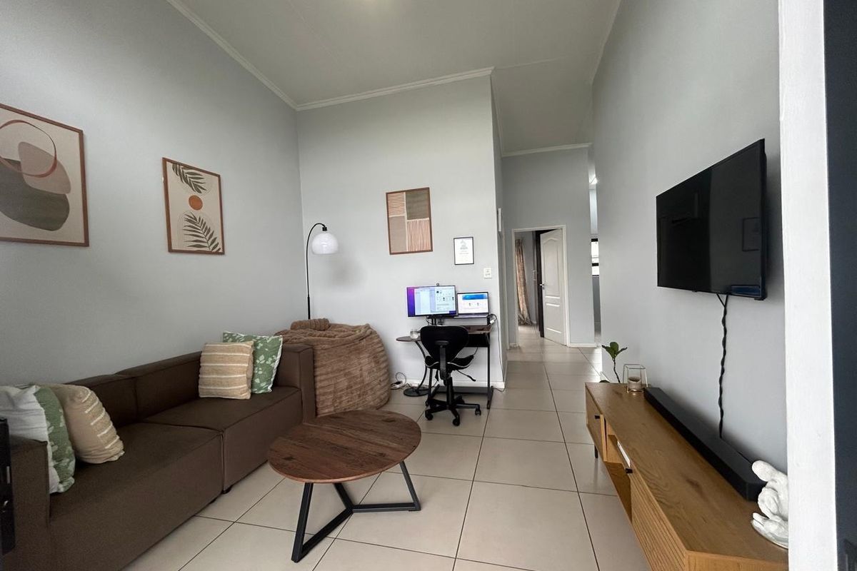 A well-maintained living room featuring neutral tiled flooring, coved ceilings, and a wall-mounted television setup.