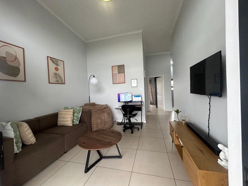 A well-maintained living room featuring neutral tiled flooring, coved ceilings, and a wall-mounted television setup.