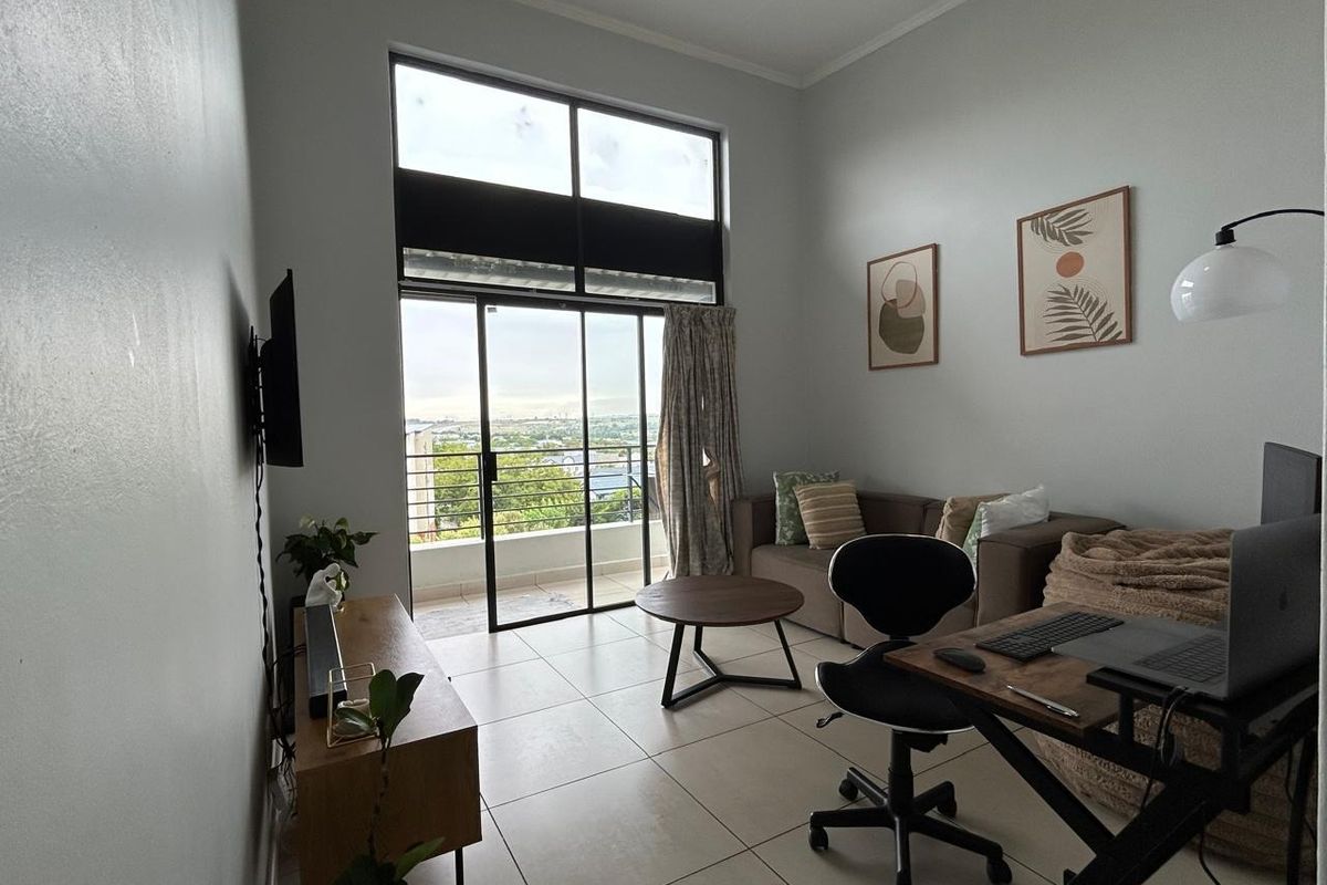 A bright living room featuring large windows, high ceilings, and direct access to a balcony with scenic views.