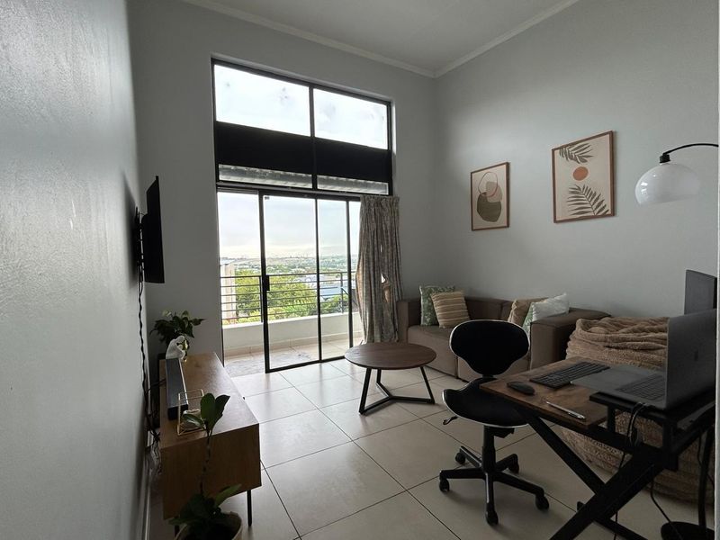 A bright living room featuring large windows, high ceilings, and direct access to a balcony with scenic views.