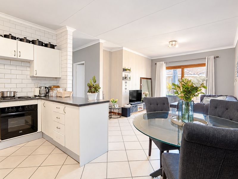 Bright open-plan living area featuring a modern kitchen with subway tile backsplash, built-in oven, and tiled flooring, flowing into a dining and lounge space.