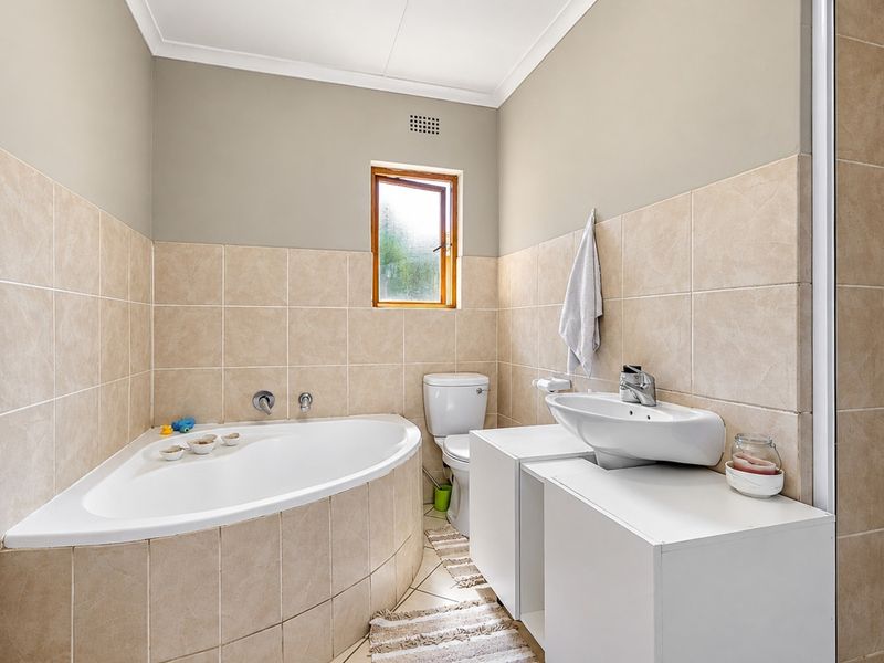 A functional bathroom featuring a corner bathtub, tiled walls, a vanity unit with a washbasin, and a toilet.