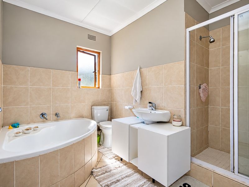 A functional bathroom featuring a corner bathtub, separate shower enclosure, vanity unit with basin, and neutral wall tiling.