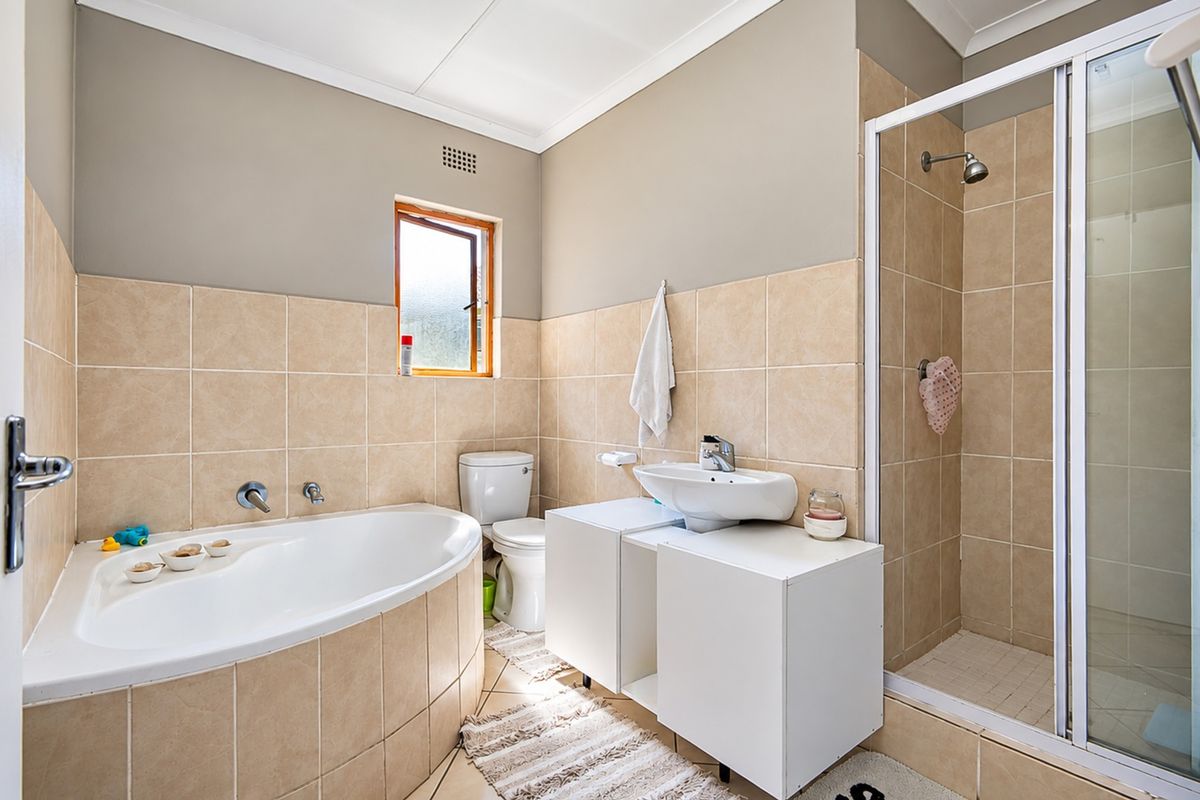 A functional bathroom featuring a corner bathtub, separate shower enclosure, vanity unit with basin, and neutral wall tiling.