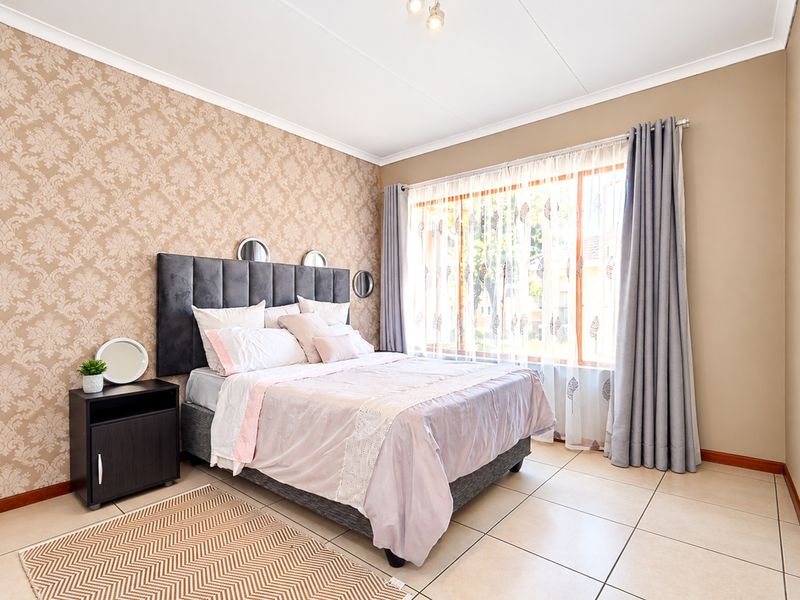 A well-lit bedroom featuring neutral tiled flooring, a patterned feature wall, and a large window with curtains.