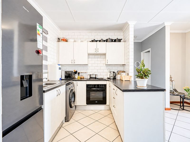 A functional kitchen featuring white cabinetry, subway tile backsplash, dark countertops, built-in oven, and tiled flooring, with an integrated laundry appliance space.