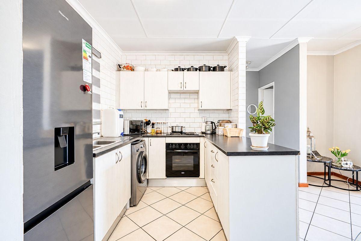 A functional kitchen featuring white cabinetry, subway tile backsplash, dark countertops, built-in oven, and tiled flooring, with an integrated laundry appliance space.