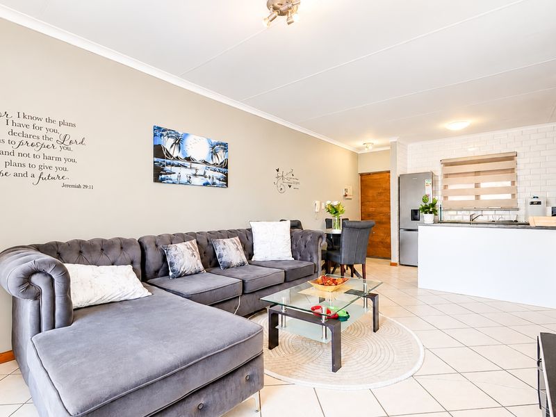 An open-plan living and kitchen area featuring tiled flooring, a modern kitchen island with a subway tile backsplash, and neutral wall finishes.