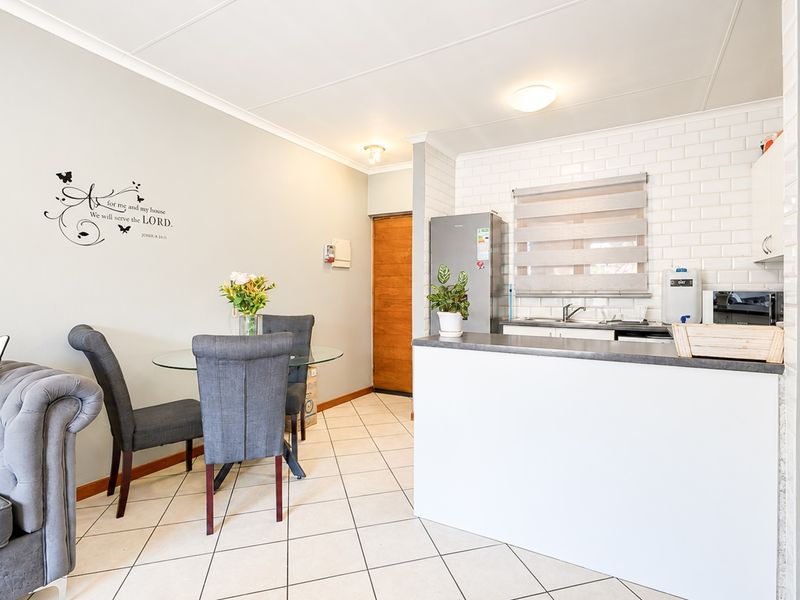 An open-plan living and kitchen area featuring tiled flooring, a modern subway tile backsplash, and functional kitchen cabinetry with a breakfast counter.