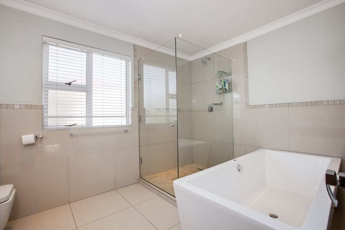 Modern bathroom featuring a glass-enclosed shower, a sleek freestanding bathtub, neutral wall and floor tiling, and natural light from a window.