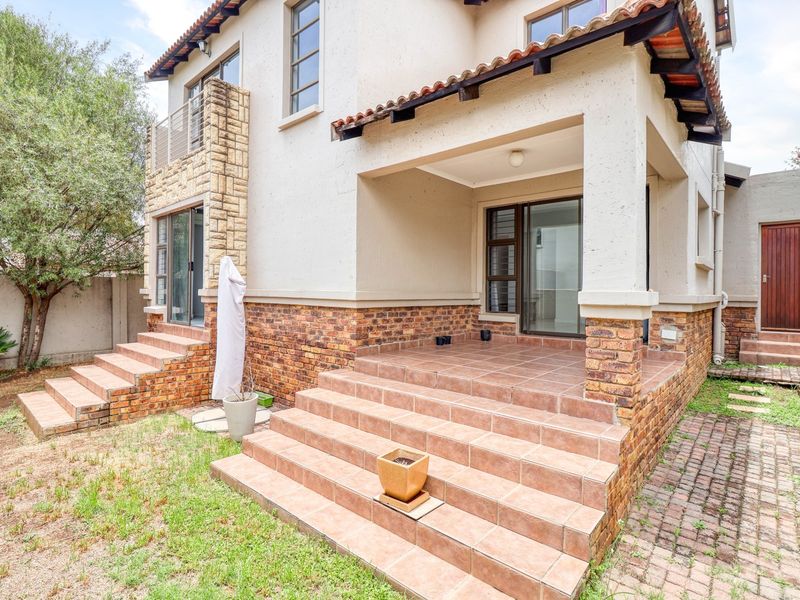 Rear view of the cluster home featuring a tiled patio, brick and stone facade, and sliding glass doors leading into the living area.