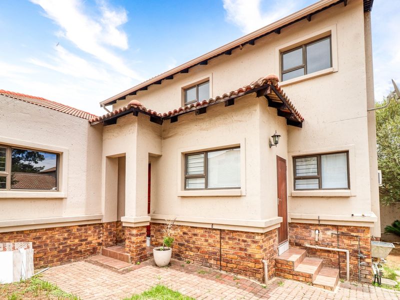 Rear view of a double-storey cluster home featuring a brick and plaster facade, tiled roof, and a paved patio area.
