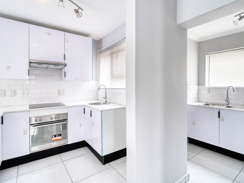 A bright, modern kitchen featuring white cabinetry, subway tile backsplash, built-in oven, electric hob, and tiled flooring with a separate scullery area.